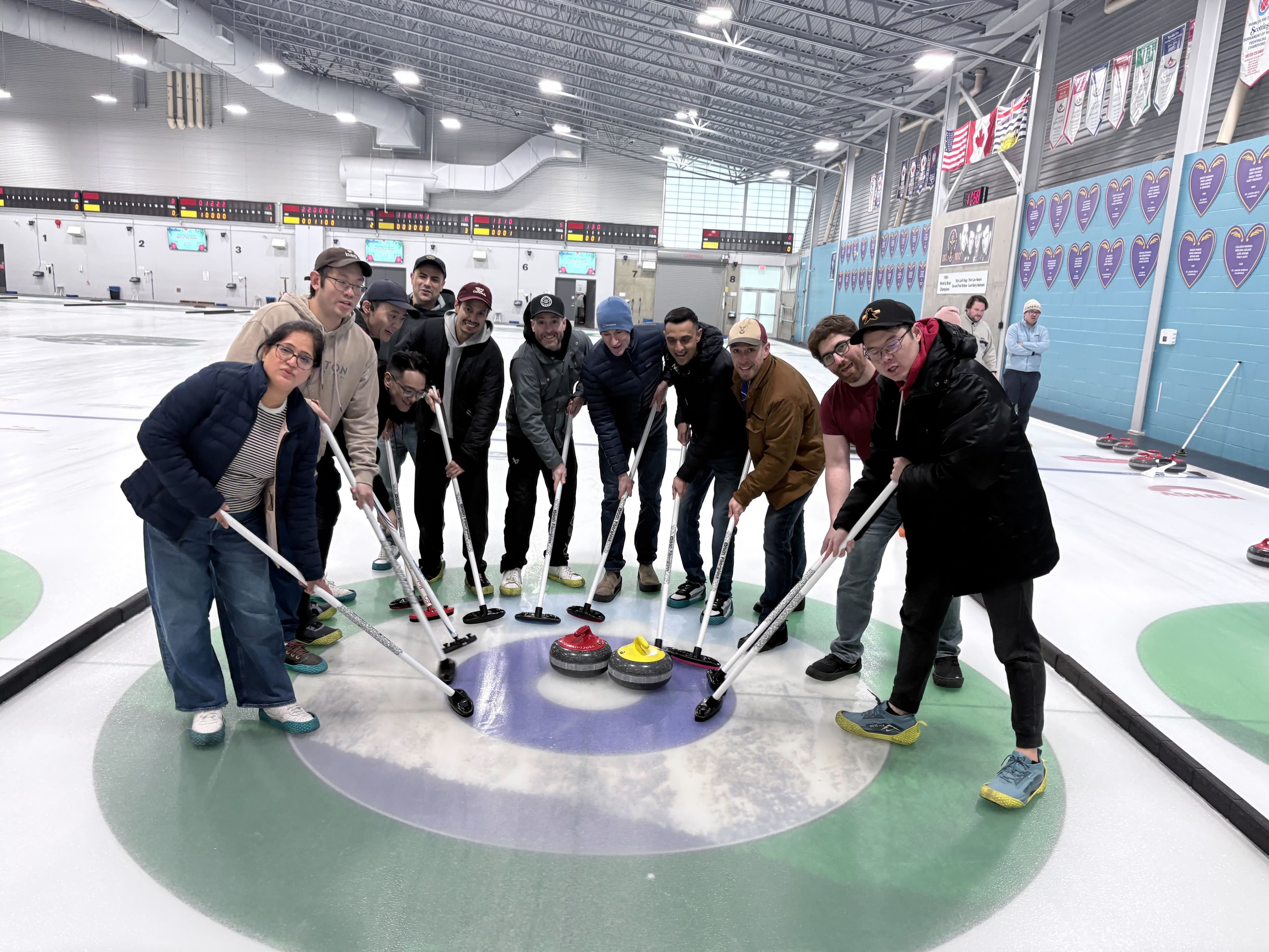 The full Betr Canada engineering team posing with curling brooms on the ice